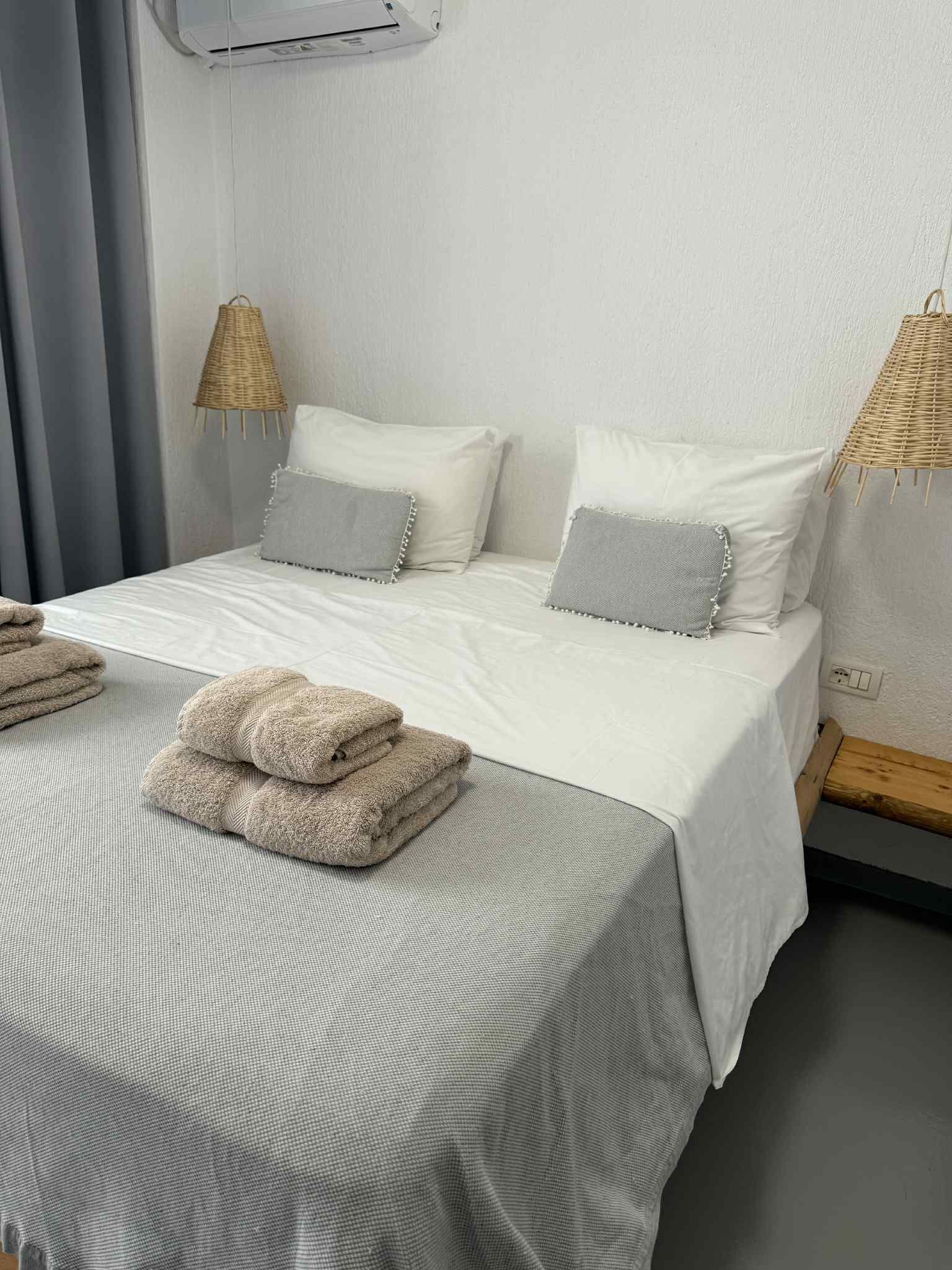 Una cama bien hecha con ropa de cama blanca y gris, dos almohadas y toallas dobladas.