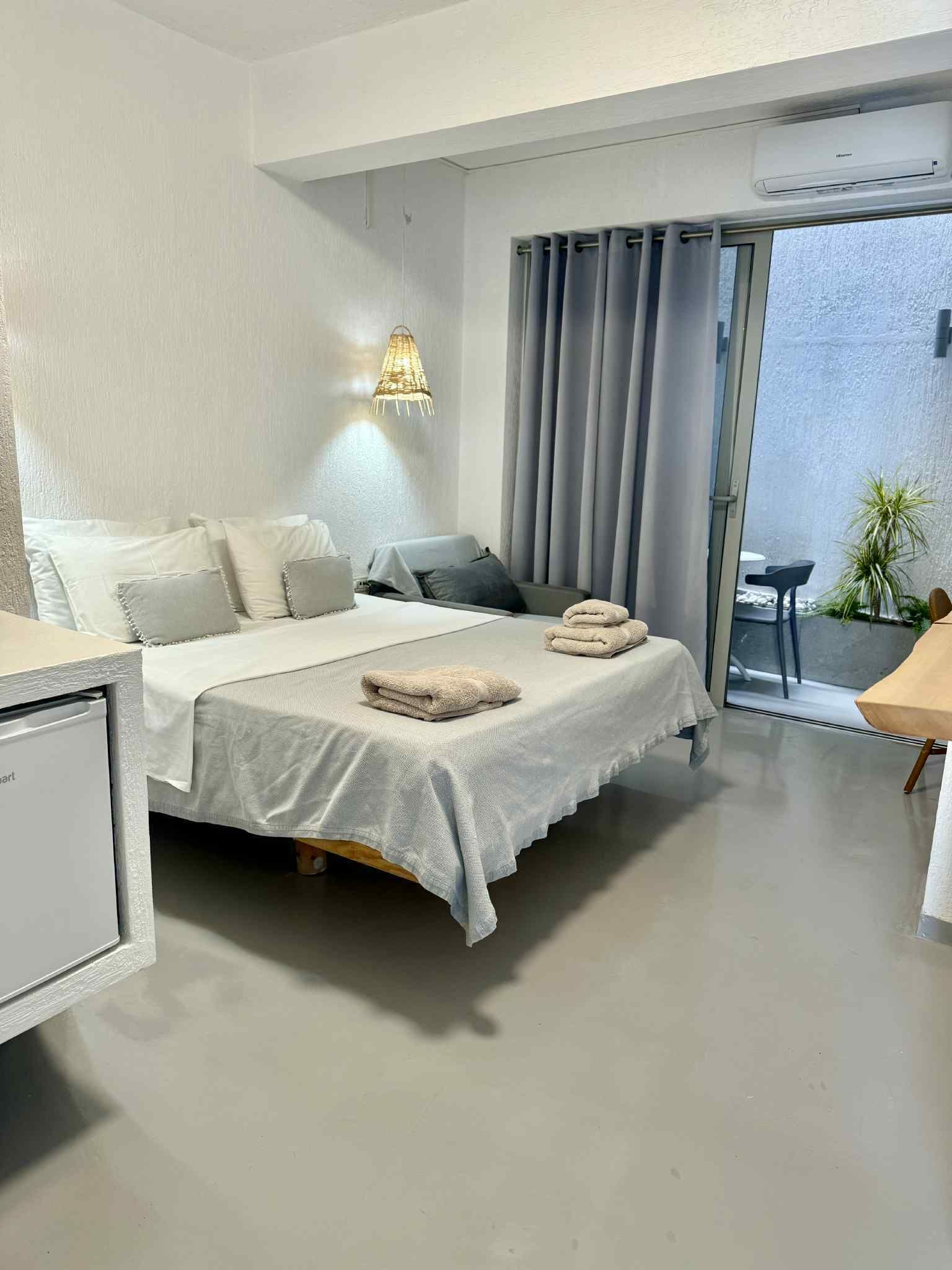 Ett modernt hotellrum med en säng, ett nattduksbord och utsikt över utomhusområdet.