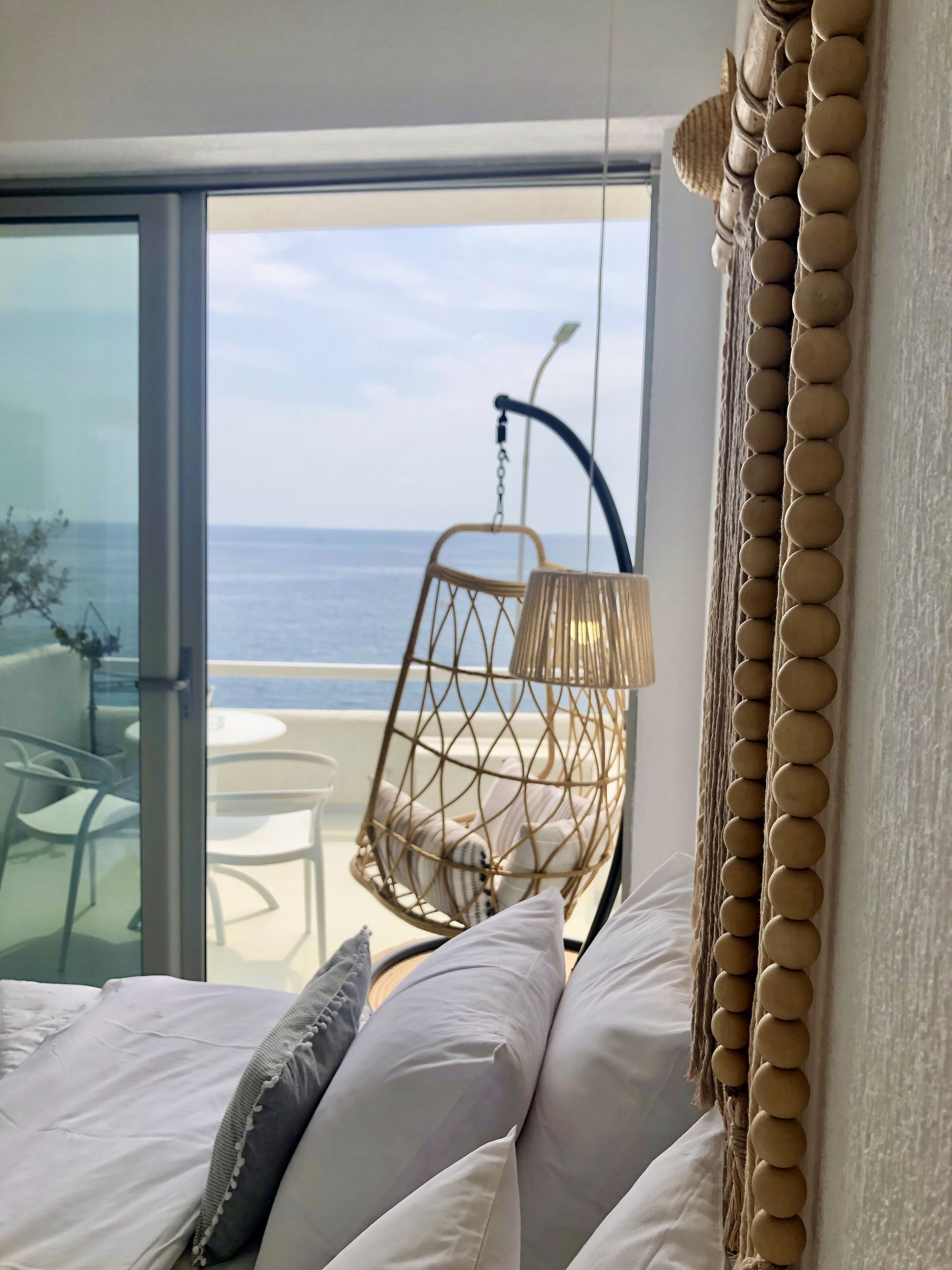 A bedroom with a bed, a hanging chair, and a view of the sea through a glass door.