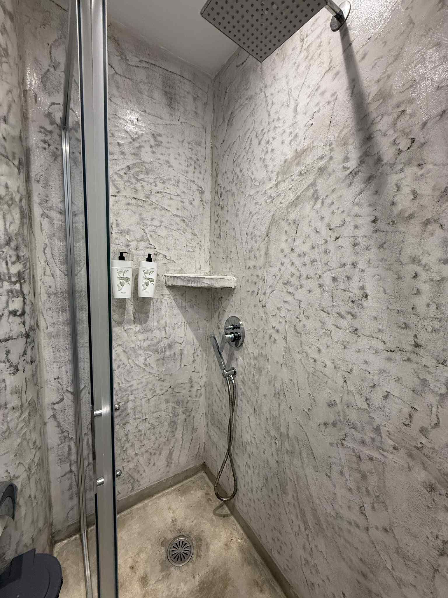 A shower with a glass door, a handheld showerhead, and a wall-mounted faucet.