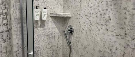 A shower with a glass door, a handheld showerhead, and a wall-mounted faucet.