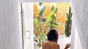 Een vrouw loopt een witte trap af naar een kamer met een stenen muur en planten.