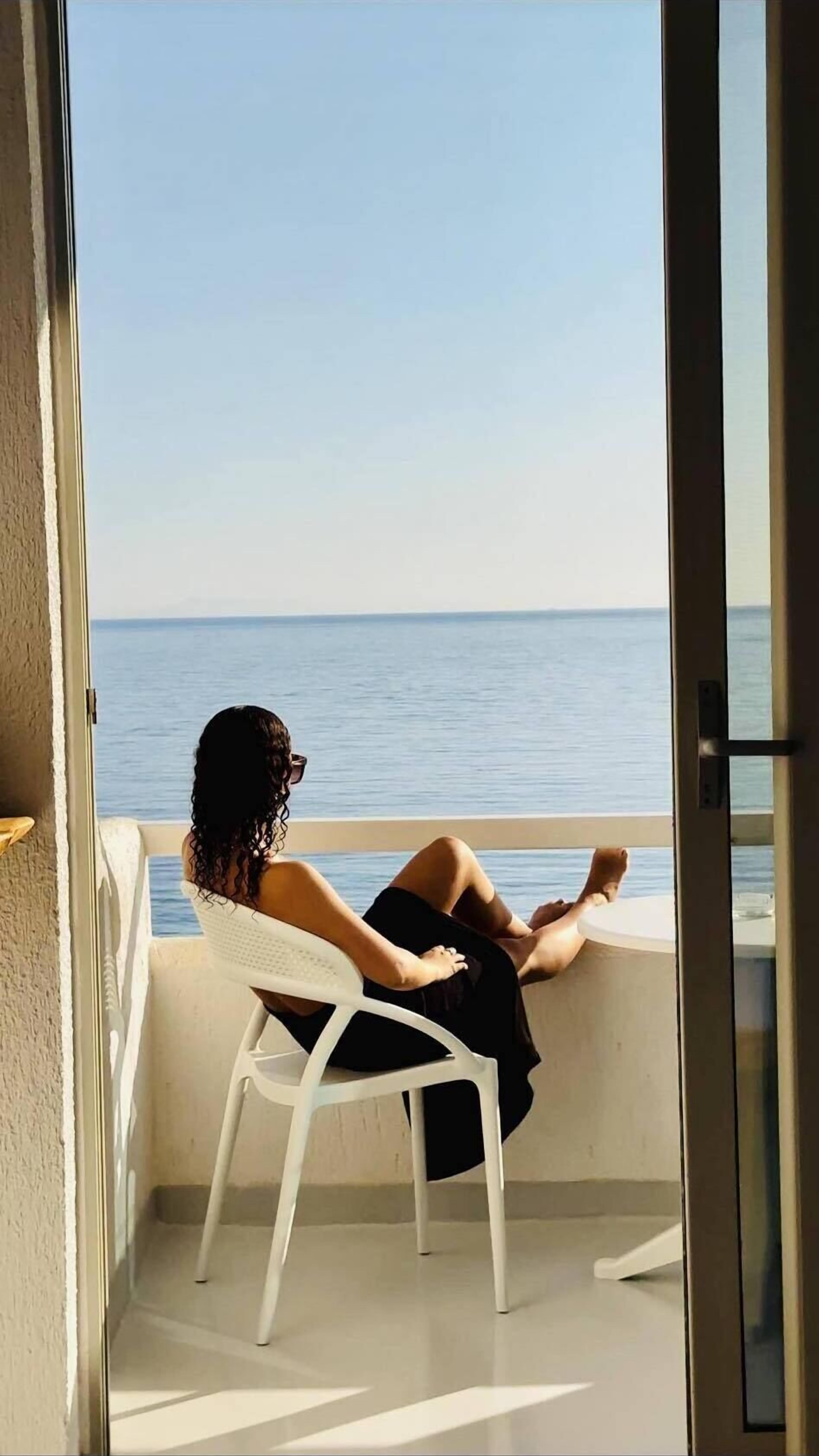 A person sitting on a white chair on a balcony overlooking a body of water.