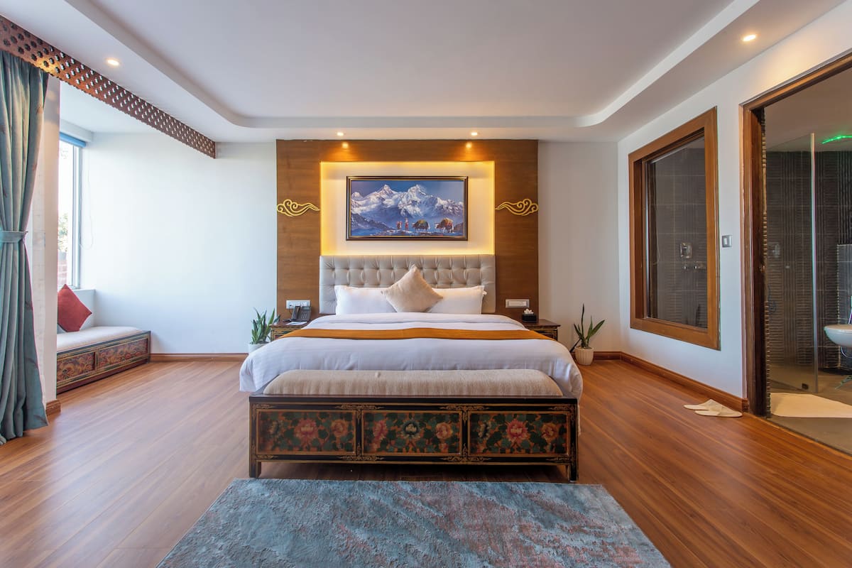 Quarto com uma cama grande, mesa de cabeceira, televisão na parede e porta de vidro deslizante para o banheiro.
