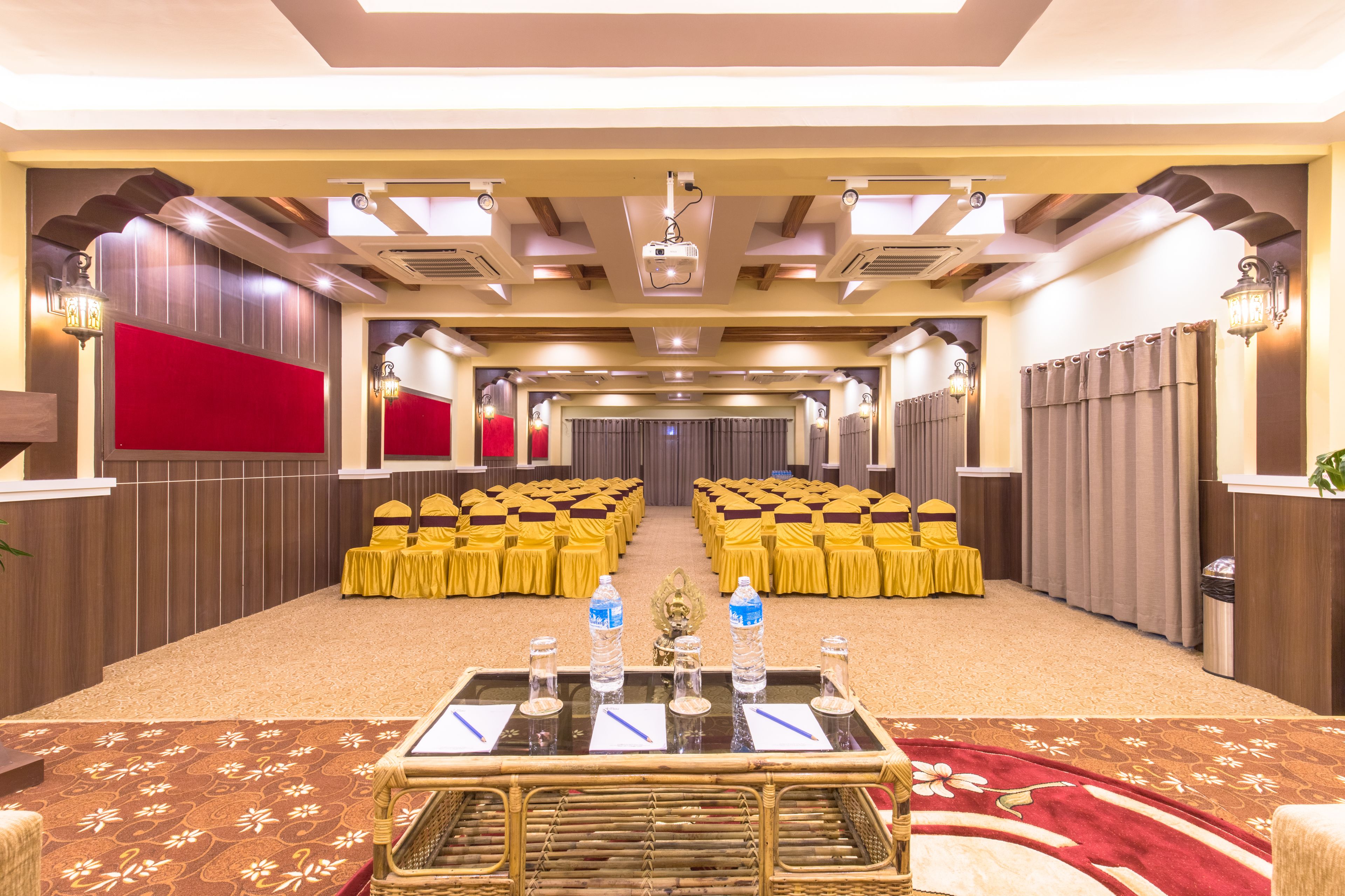 A conference room with rows of yellow chairs, a podium with water bottles, and a carpeted floor.