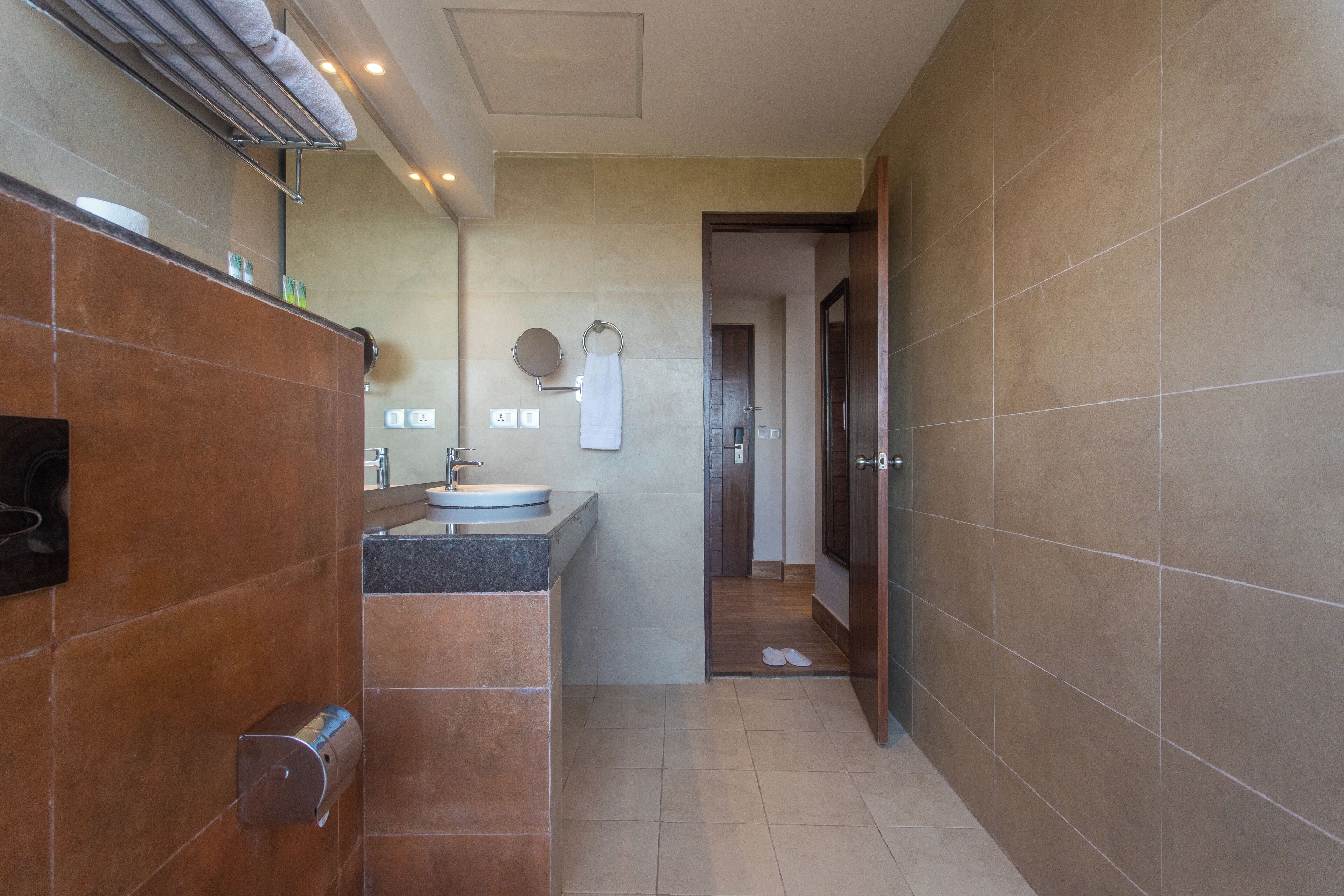 Un baño moderno con lavamanos, espejo, toallero y una puerta que da a otra habitación.