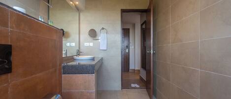 Un baño moderno con lavamanos, espejo, toallero y una puerta que da a otra habitación.