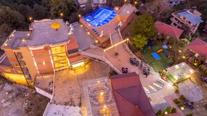 An aerial view of a resort with multiple buildings, a swimming pool, and outdoor seating areas. - Hotel Sarathi (Dhulikhel)