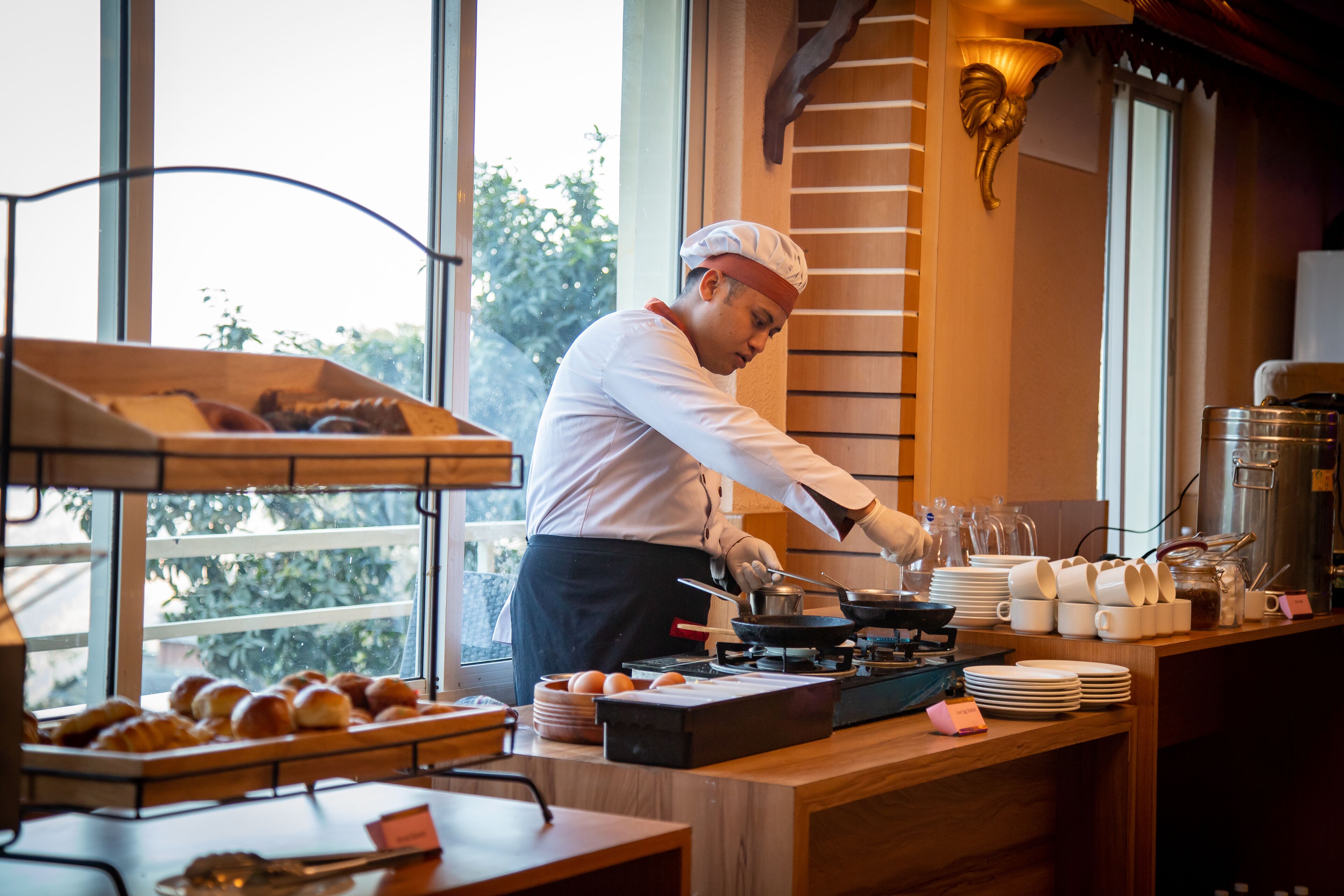 A chef cooking in a kitchen with a view of trees outside.