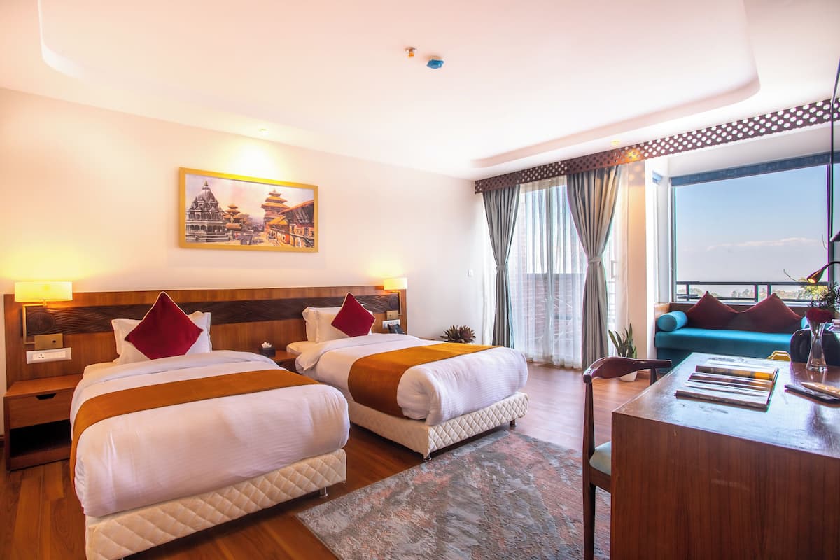 Quarto de hotel com duas camas, uma escrivaninha e uma janela grande com vista.