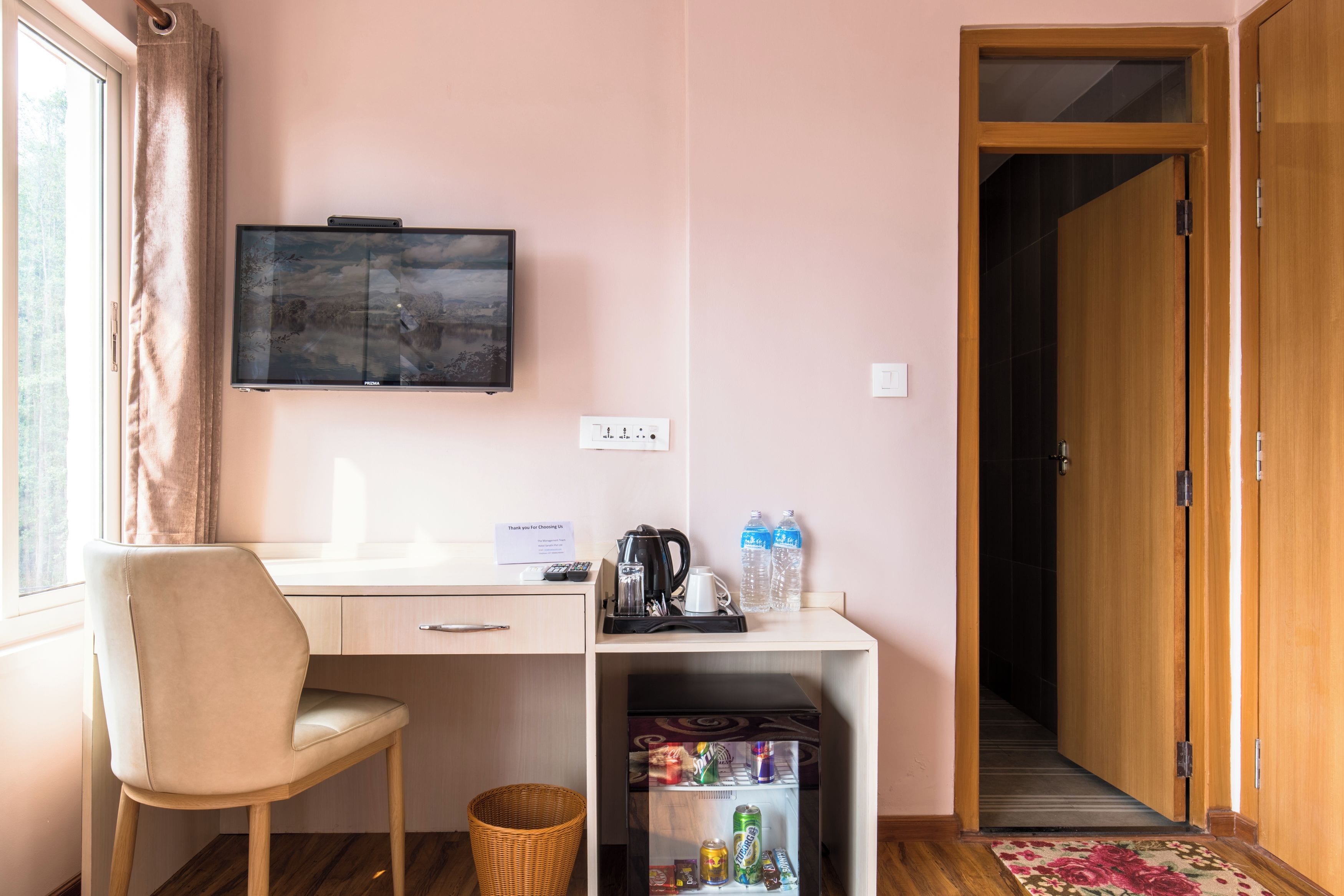 A room with a desk, chair, television, and a small refrigerator with beverages.