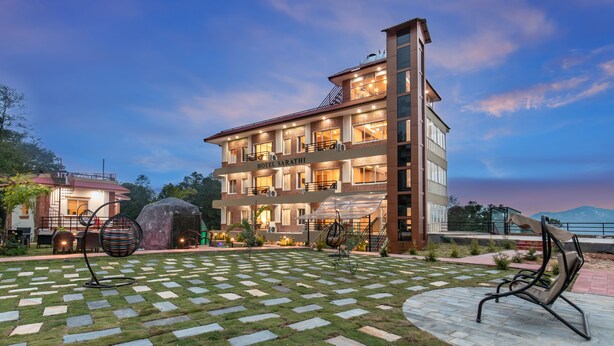 A hotel with a modern design, featuring a well-lit entrance and a spacious outdoor area with a checkered pattern of grass and stone tiles. - Hotel Sarathi (Dhulikhel)