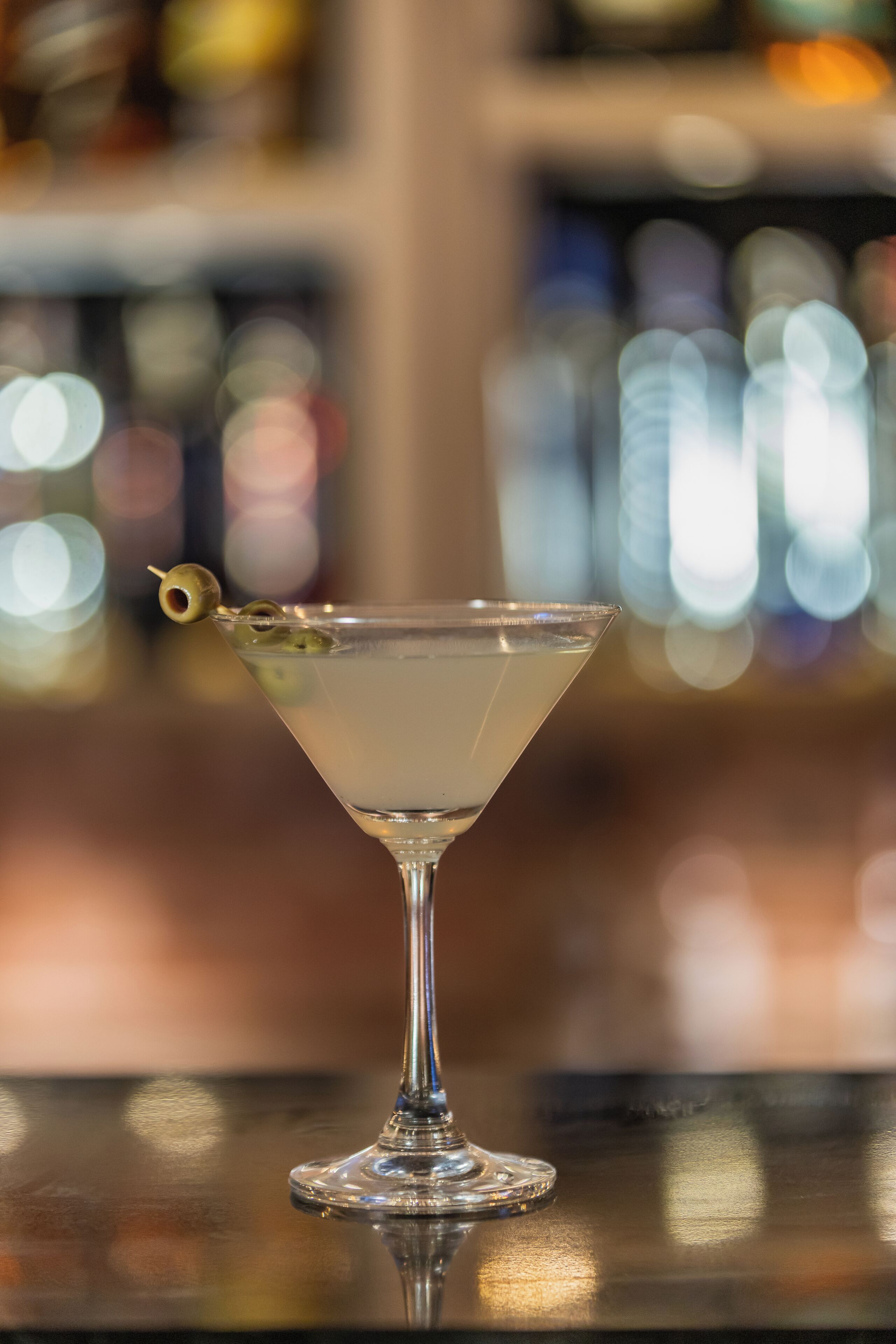 Una copa de martini con aceituna sobre una barra.
