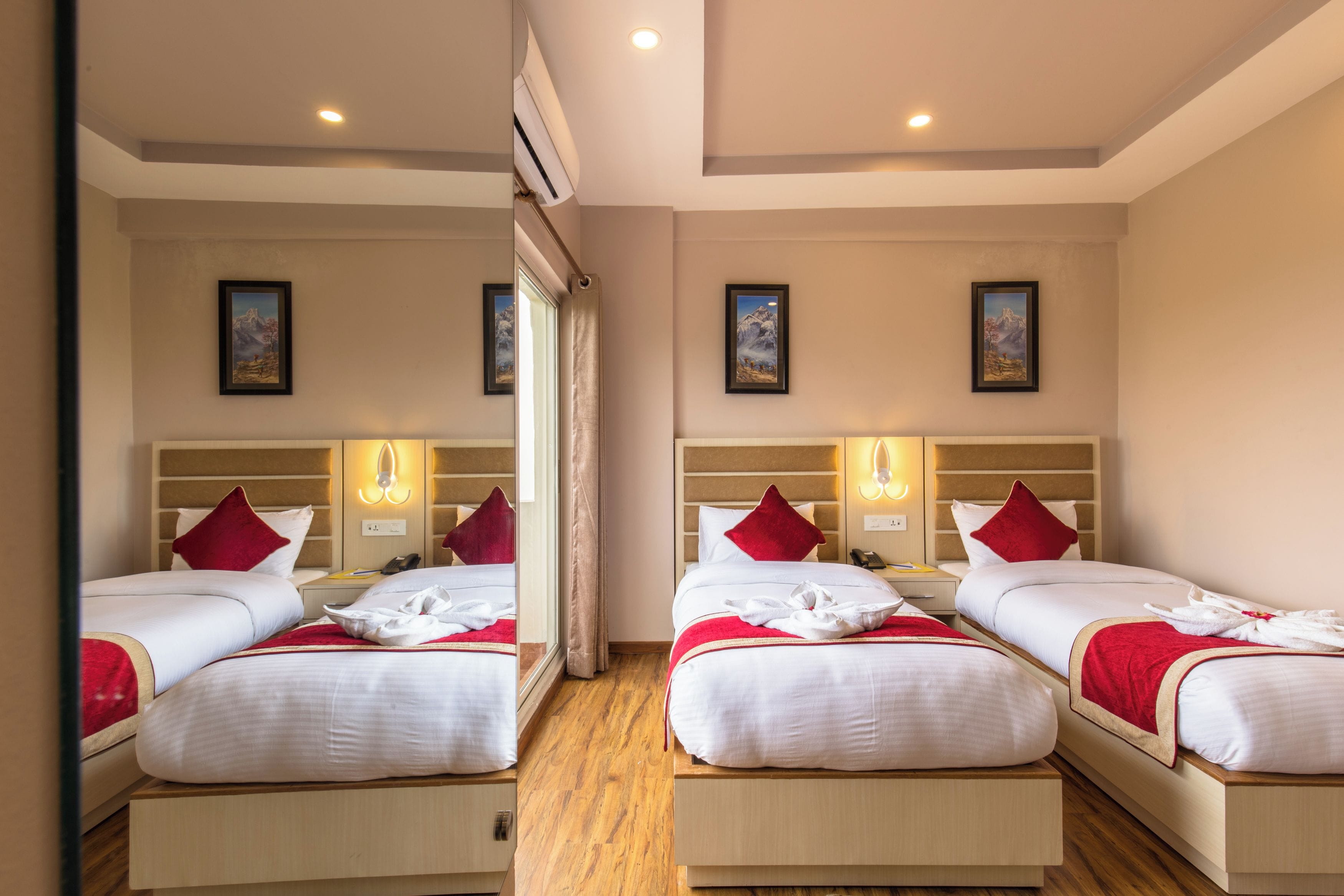 Une chambre d’hôtel avec deux lits, chacun agrémenté d’un coussin rouge, de lampes de chevet et d’œuvres d’art encadrées accrochées aux murs.