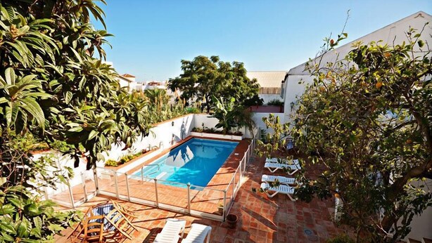 A rectangular swimming pool with a tiled deck, surrounded by white walls and lush greenery. - Hostal La Posada de Conil (Conil de la Frontera)