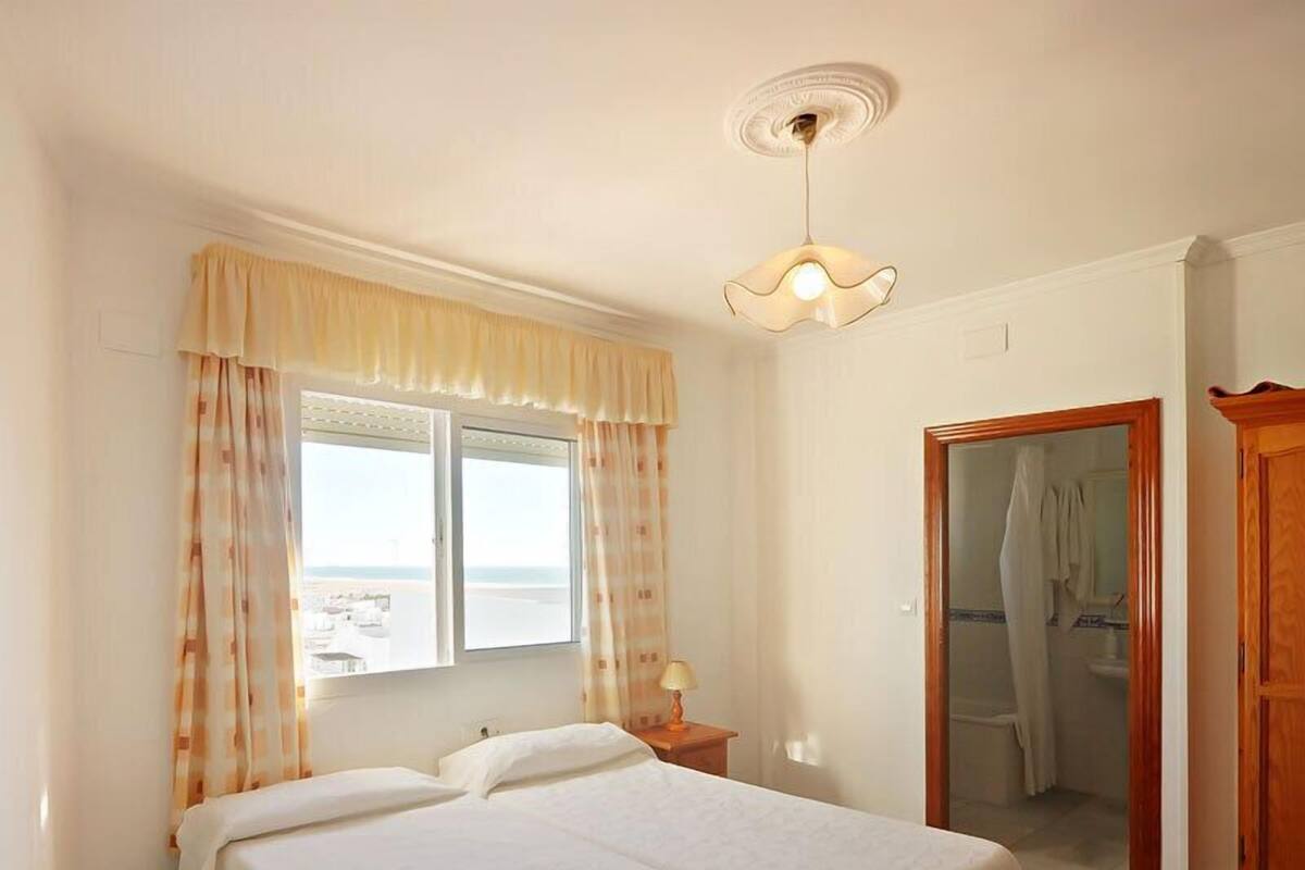 A bedroom with two beds, a window with curtains, a bedside lamp, and a wooden wardrobe.