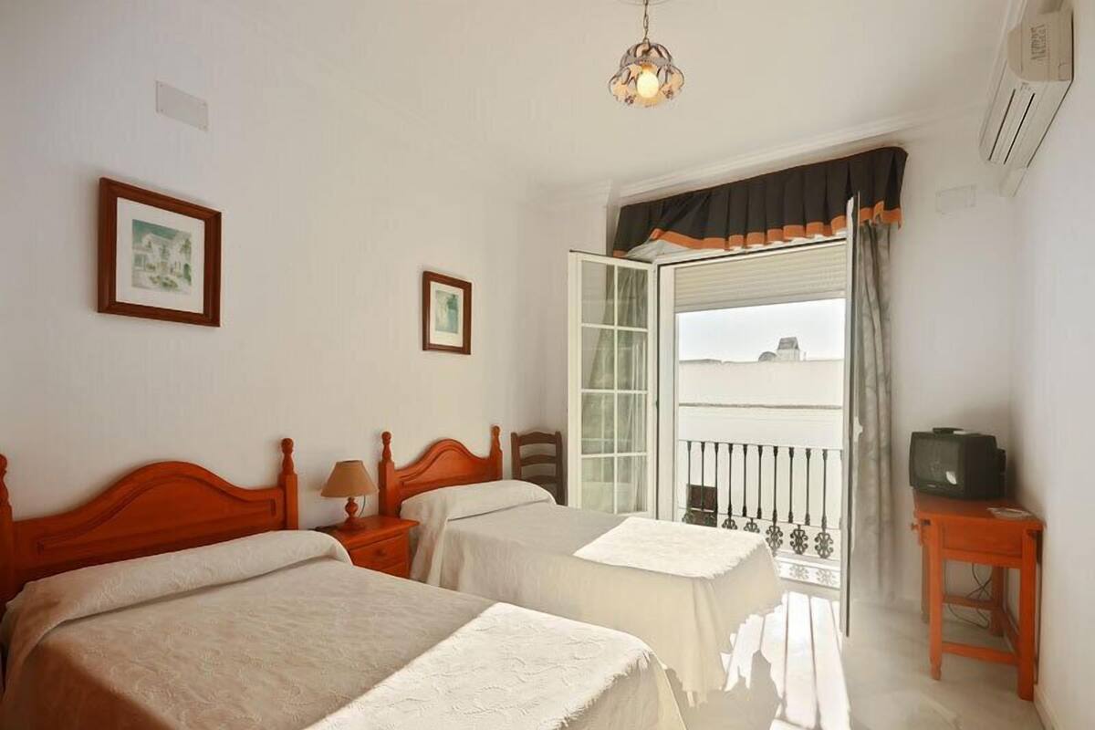 A hotel room with two beds, a balcony with a view, a television, and a lamp.