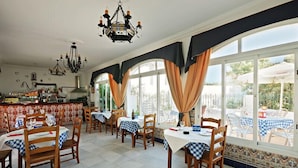 A dining area with tables set for two, wooden chairs, and a chandelier. - Hostal La Posada de Conil (Conil de la Frontera)