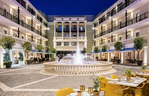 Un patio de hotel con una fuente central, mobiliario exterior y varios balcones.