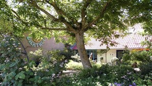 A garden with a tree, a building with a sign, and a fence. - Gästehaus und Cafe - Lichthof (Gaedheim)