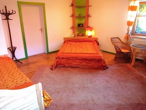 A room with a bed, a chair, a table, a shelf with decorative items, and a door. - Gästehaus und Cafe - Lichthof (Gaedheim)