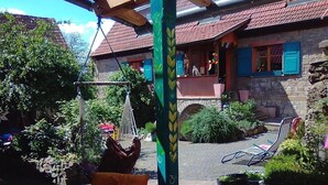 A courtyard with a stone wall, a hammock, and a wicker chair with a yellow cushion. - Gästehaus und Cafe - Lichthof (Gaedheim)