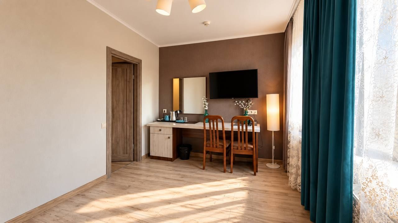 Habitación de hotel con escritorio de madera, una silla, televisor, lámpara y ventana con cortinas.