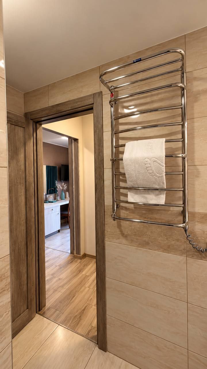 Een gang met een handdoekrek aan de muur, een houten deurkozijn en een glimp van een badkamer met een wastafel en spiegel.