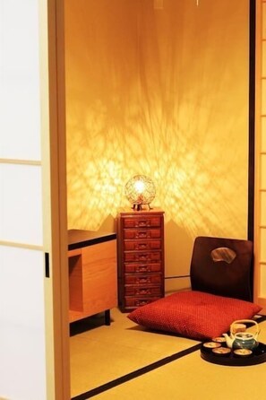 A traditional Japanese room with tatami flooring, a low wooden dresser, a red cushion, and a small table with a teapot and cups. - Kyoto Nijo Machiya (Kyoto)