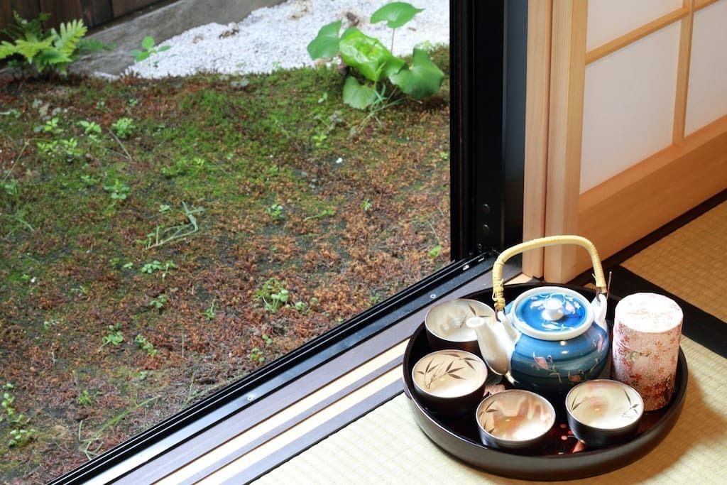 A tray with a teapot, cups, and a candle on a tatami mat near a window.