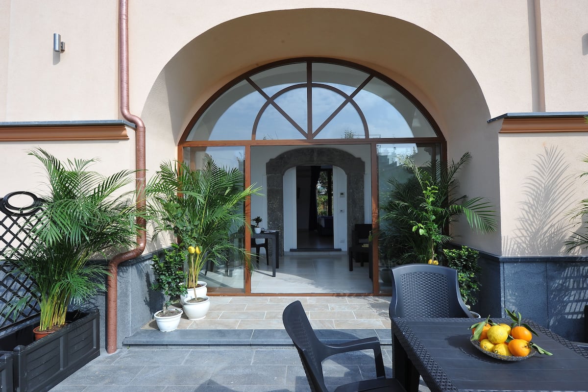 An outdoor patio area with a table and chairs, potted plants, and a glass entrance leading to an interior space.