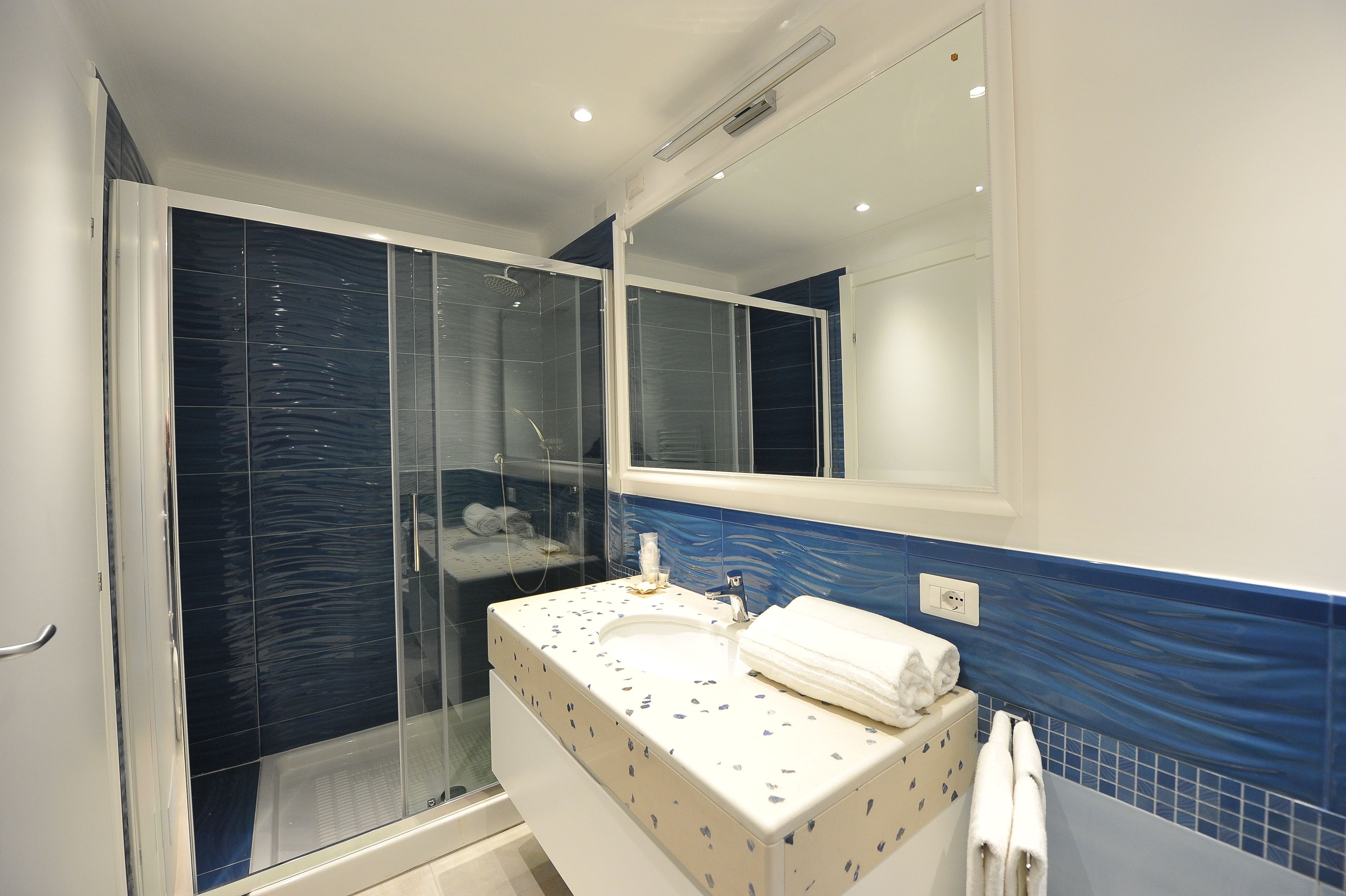 Un baño con ducha de vidrio, un lavabo blanco con detalles azules y un espejo encima.