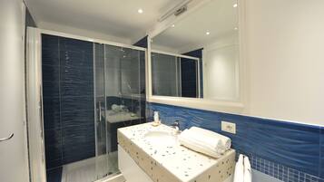 Un baño con ducha de vidrio, un lavabo blanco con detalles azules y un espejo encima.