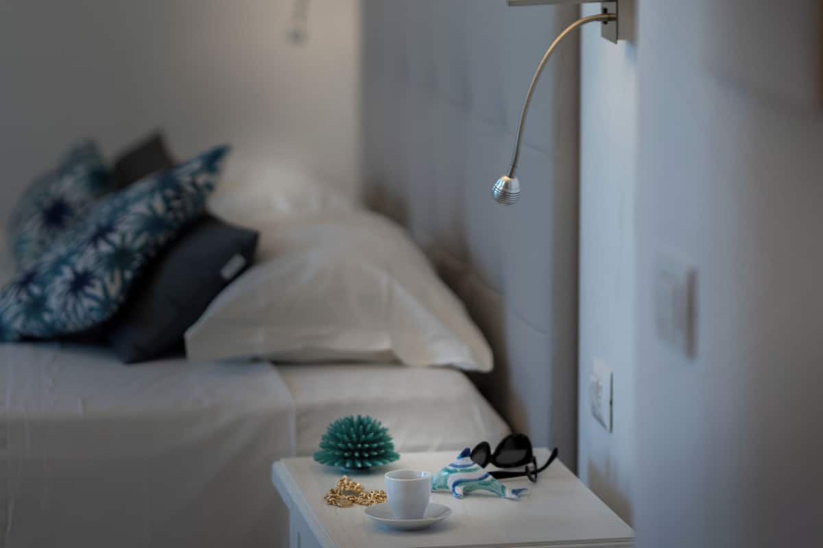 A neatly arranged bedroom with a bed, bedside lamps, a small table with a cup, and a decorative pine cone.