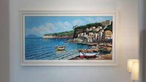 Une chambre à coucher avec un lit, des oreillers, une table de chevet et un tableau encadré représentant un paysage côtier.