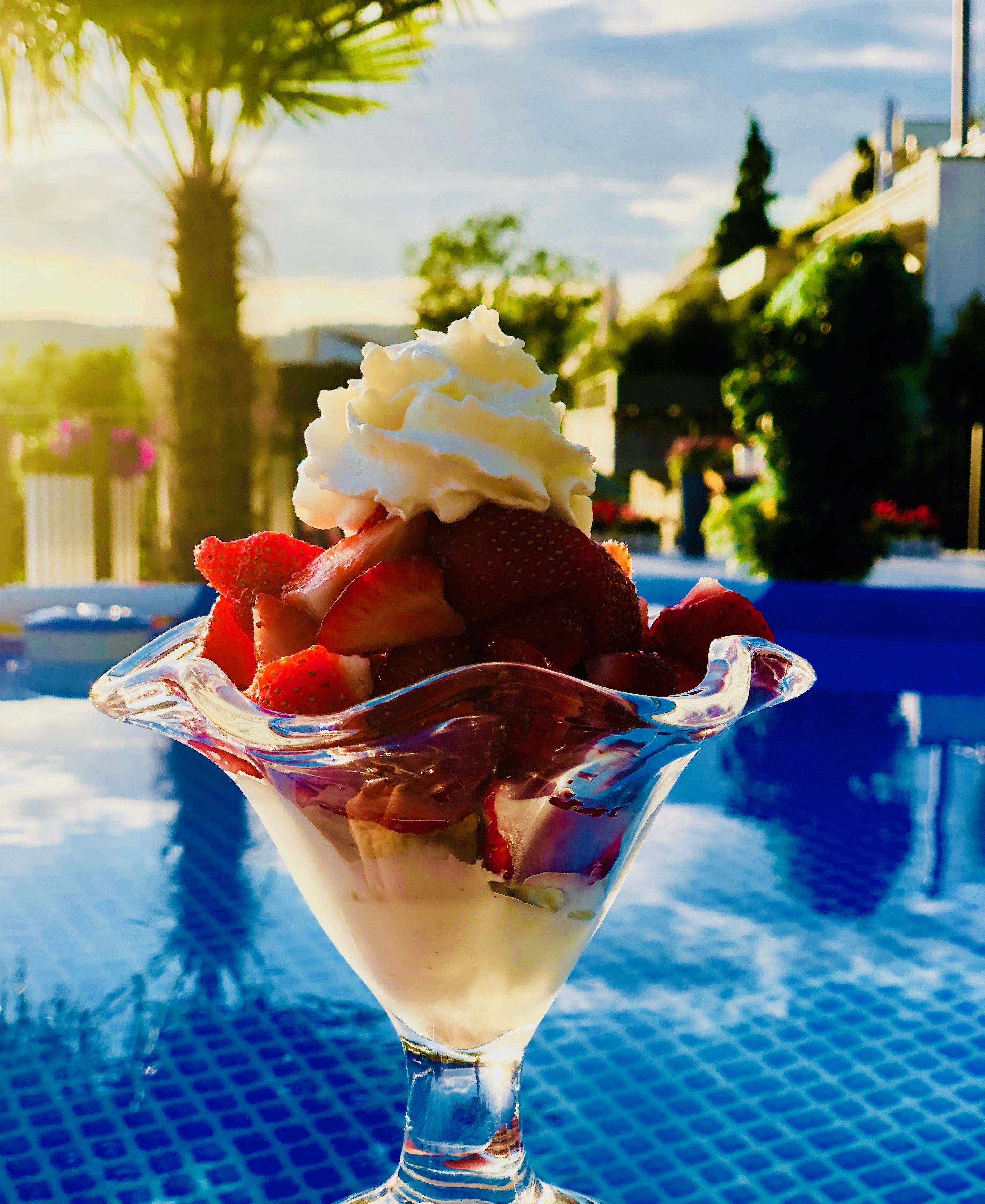 Un postre en un bol de cristal sobre una mesa junto a la piscina.