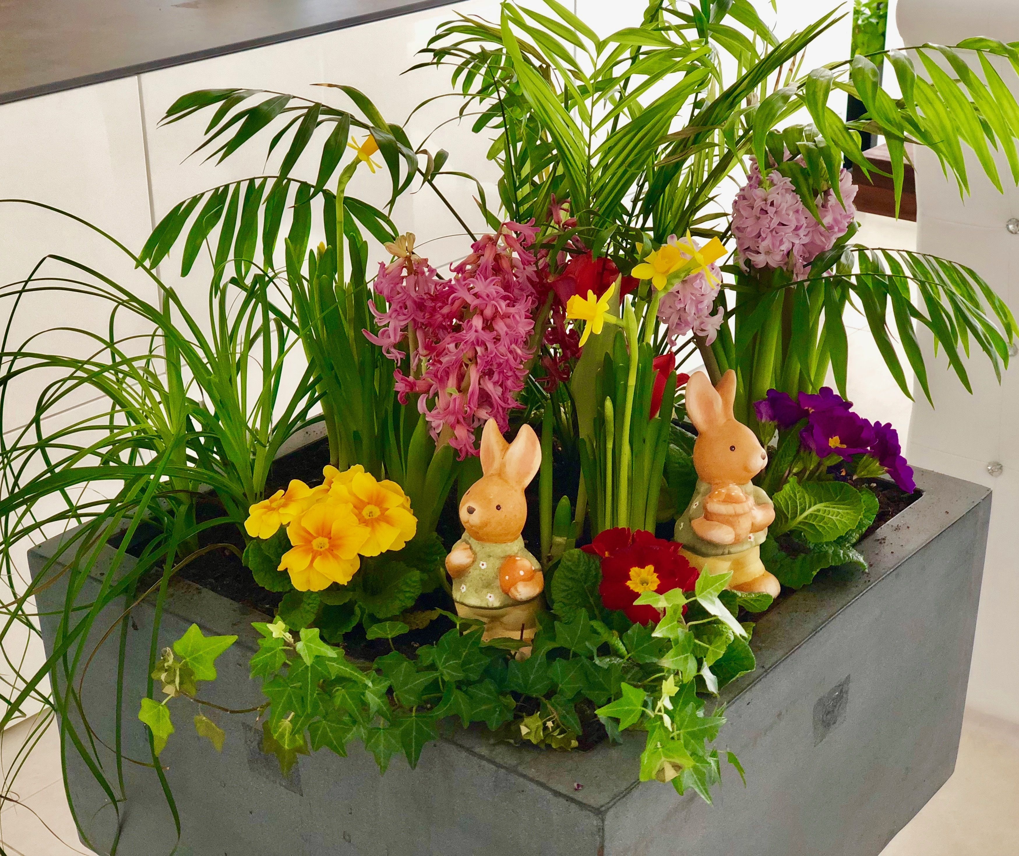 Ein Blumentopf mit verschiedenen Blumen und einer Hasenfigur.