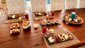 A breakfast buffet with various food items and drinks on a wooden table, surrounded by white cushioned chairs. - perfect lifestyle Design Boutique & Private SPA (Gebenstorf)