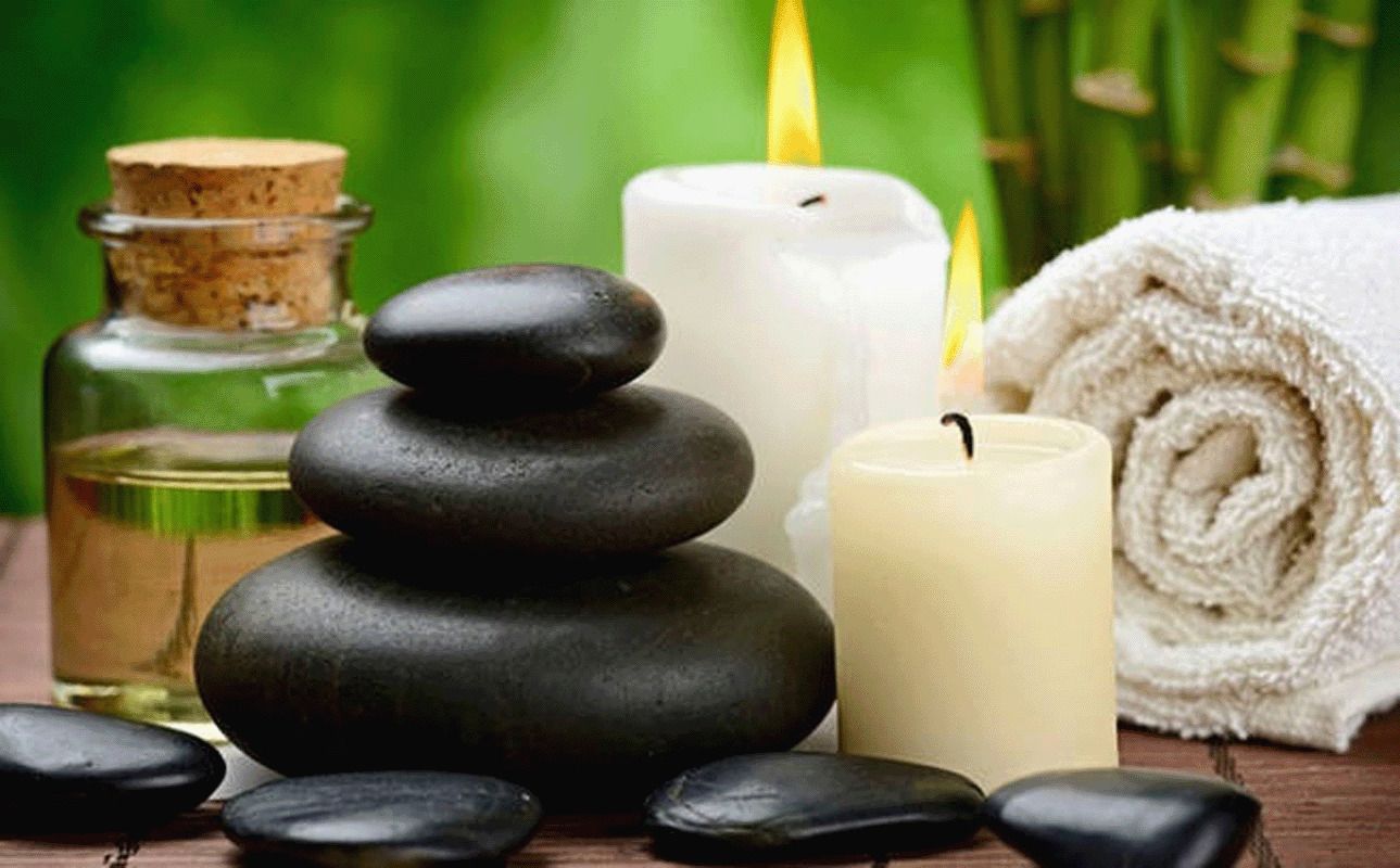 A stack of black stones, a white candle, a rolled white towel, and a glass bottle with a cork.