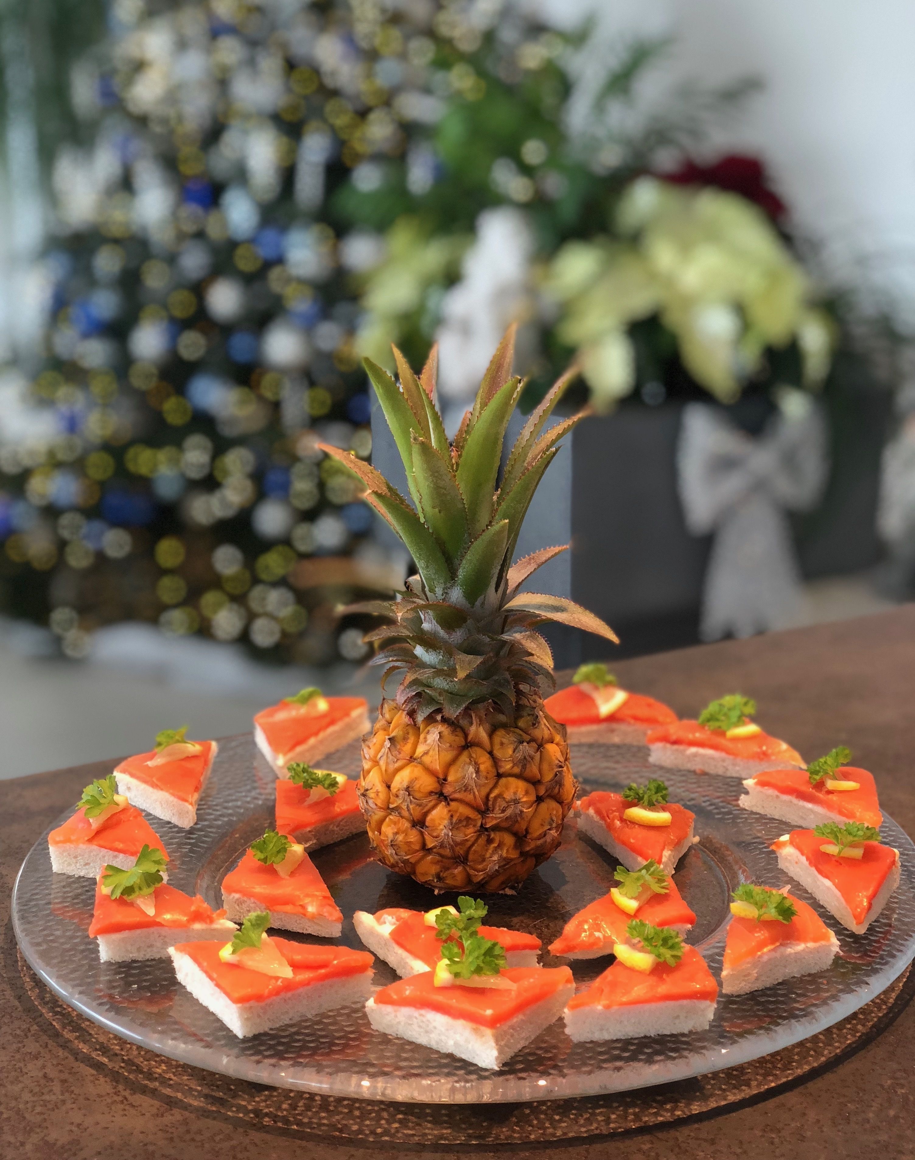 Eine Ananas als Mittelpunkt, umgeben von Lachs belegten Toastscheiben auf einer Glasschale.