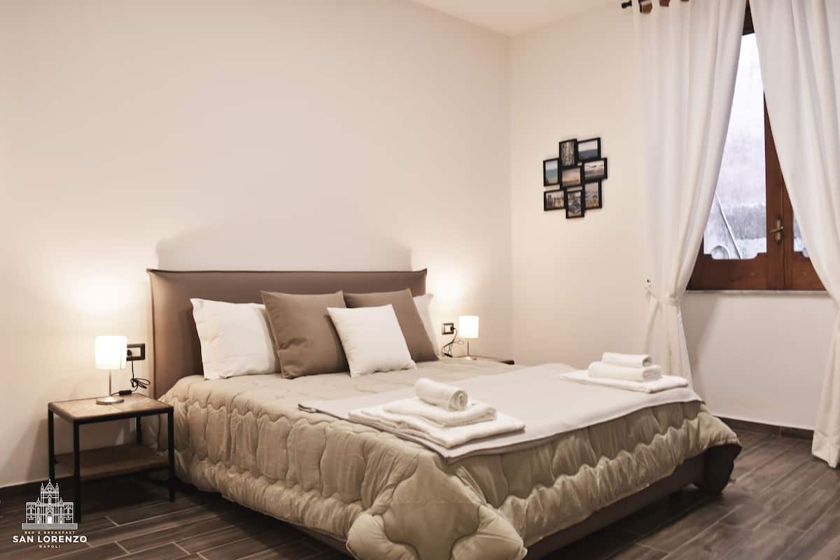 A hotel room with a large bed, two bedside tables, a wall-mounted light, and a window with curtains.