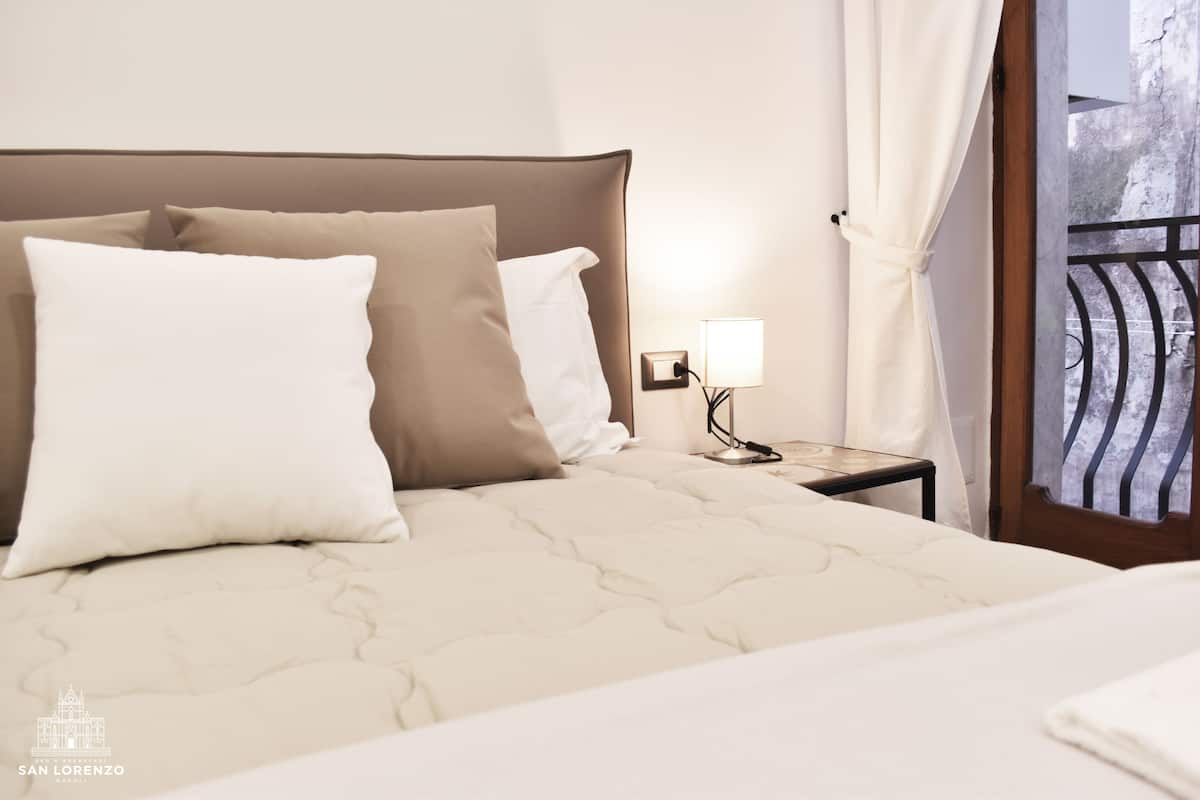 A neatly made bed with a headboard, a bedside lamp, and a view of a balcony with a railing.