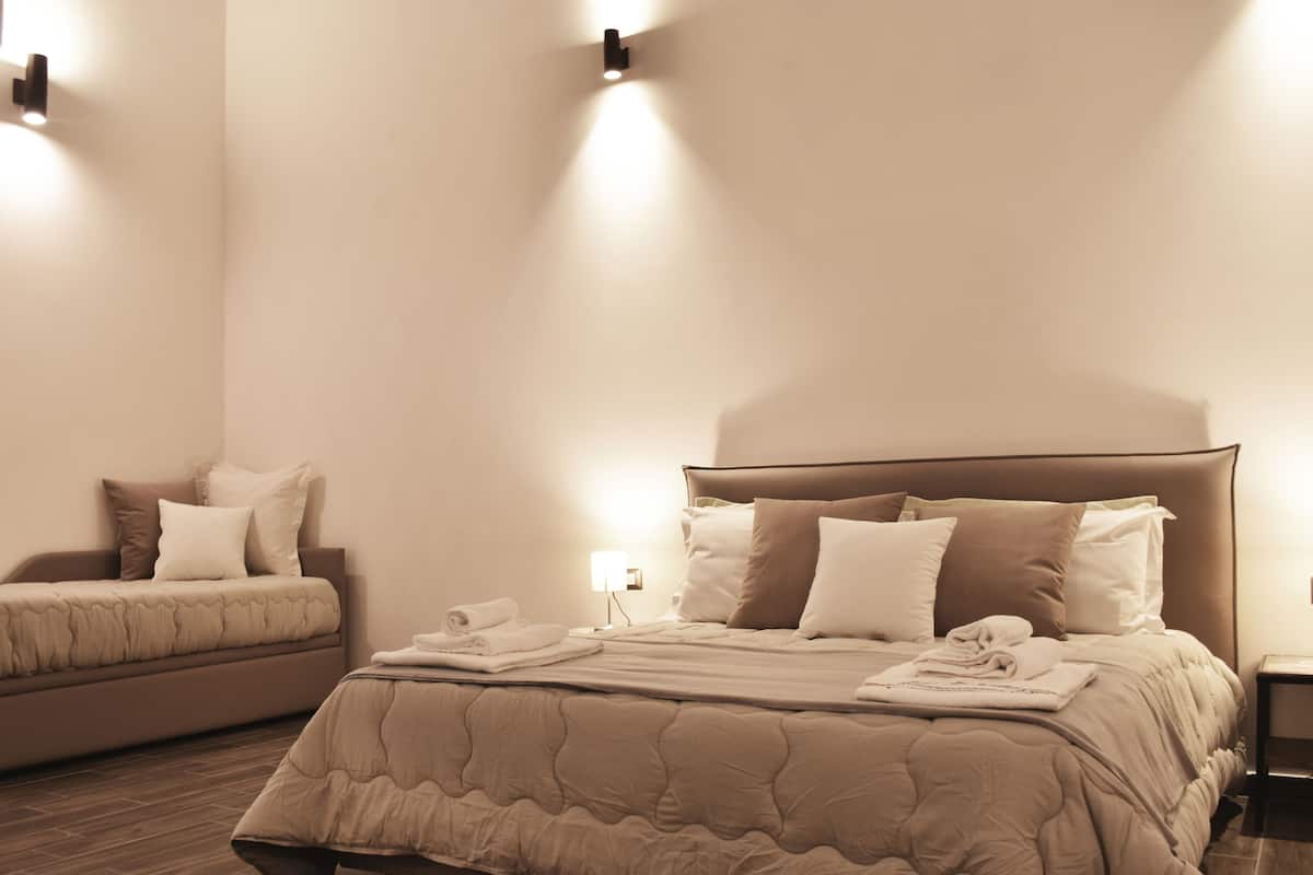 A bedroom with a large bed, a smaller sofa, and a nightstand with a lamp.
