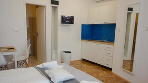 A hotel room with a bed, a desk, a small kitchenette, and a bathroom.
