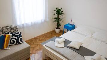 A hotel room with a bed, a bedside table, a chair, a potted plant, and a window with curtains.