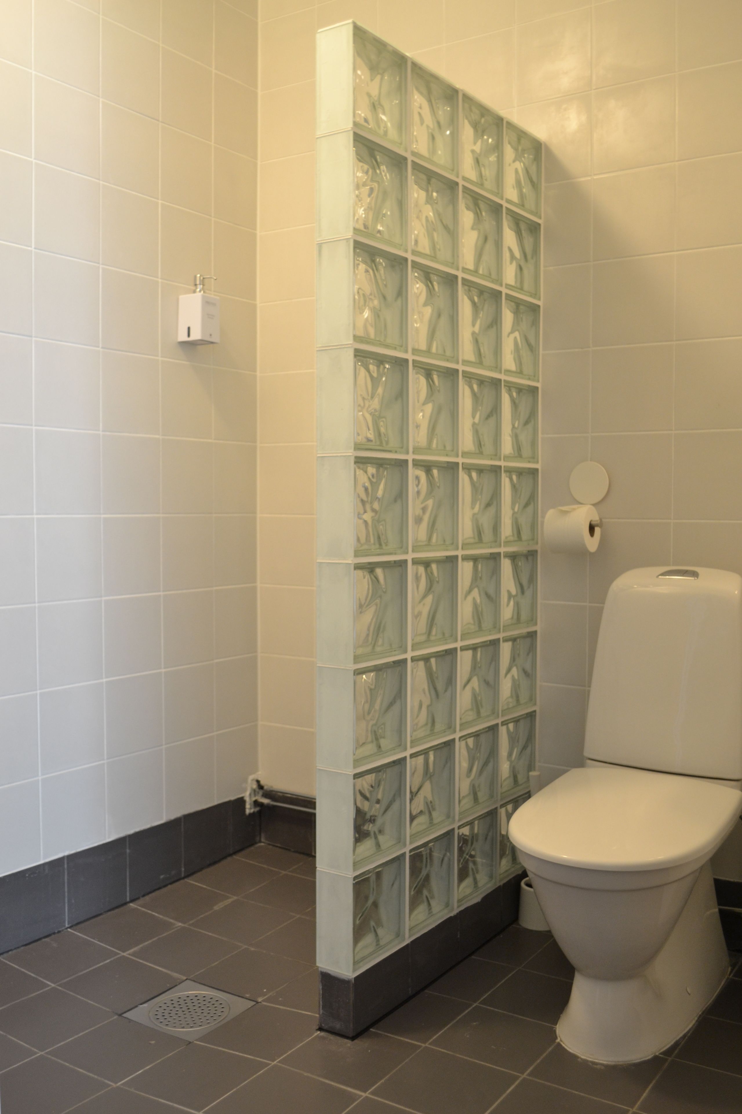Un baño con inodoro, separador de vidrio y secador de manos.