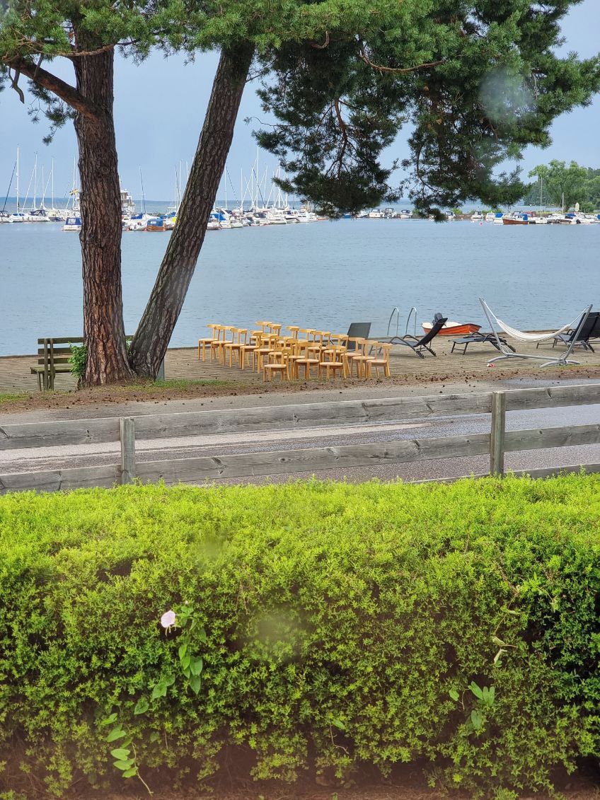 A beach with a row of chairs and a hammock, a large tree, and a view of boats in the water.