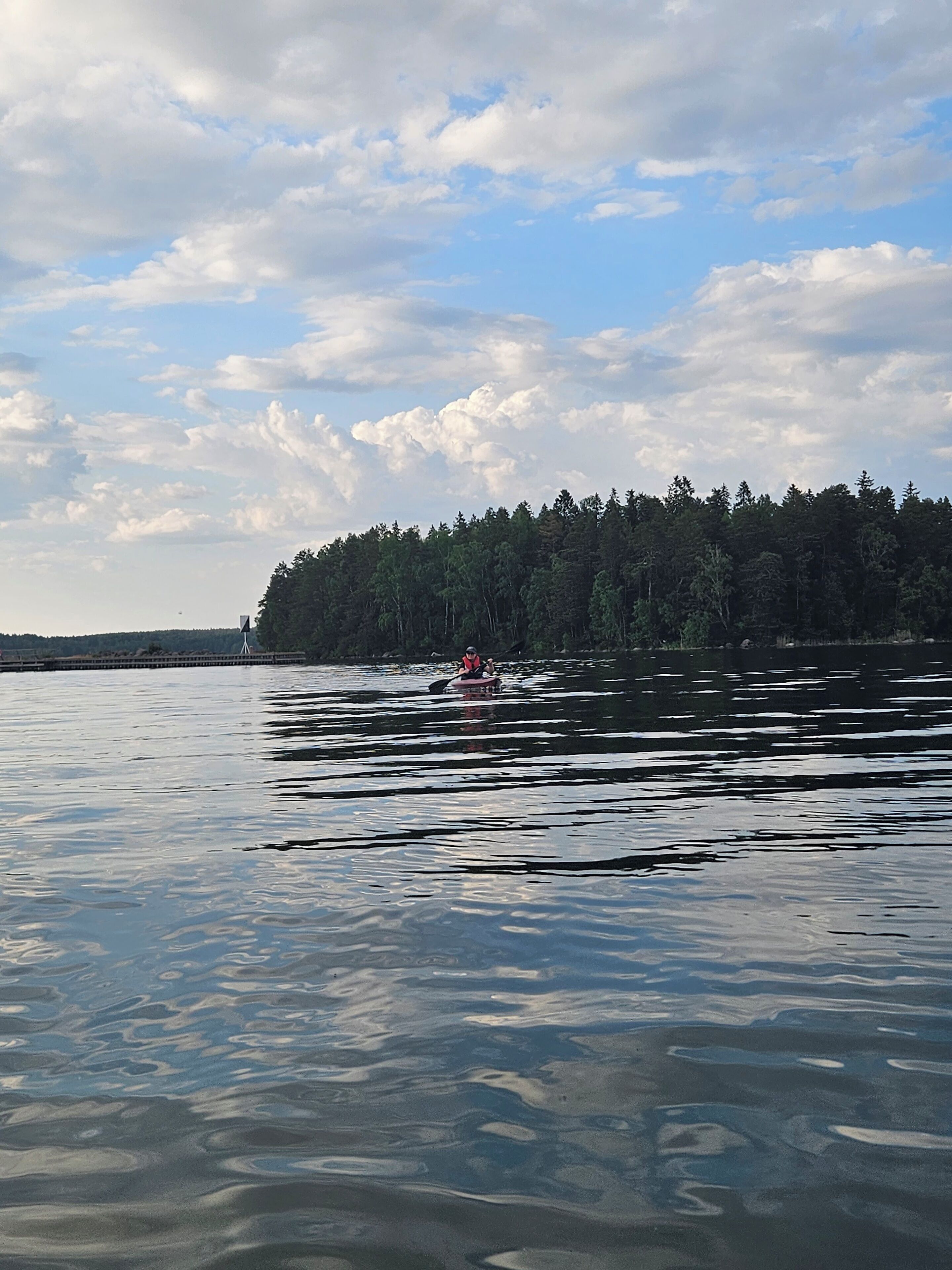 Un lago tranquilo con un kayak en primer plano y una isla boscosa al fondo.
