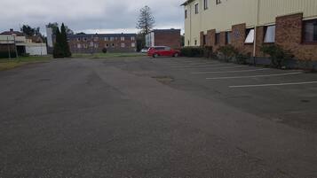 A parking lot with a red car parked in the distance, surrounded by buildings with brick and metal exteriors.