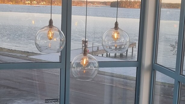 A room with large windows overlooking a body of water, featuring three hanging light fixtures. - Hotell Wettern (Karlsborg)